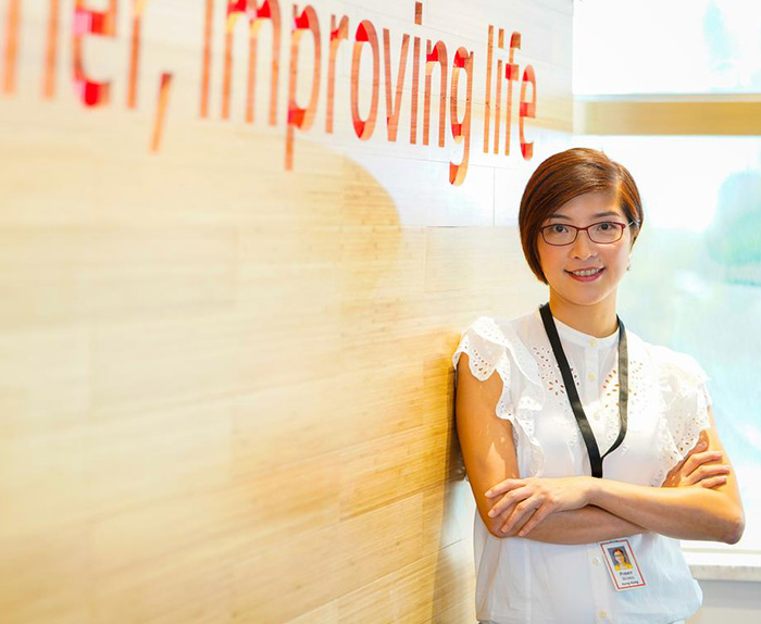 An Associate standing in front of a wall that says Together, improving life.